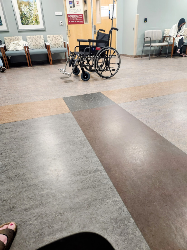 A somewhat empty waiting room. An empty wheelchair sits in the middle of the floor.