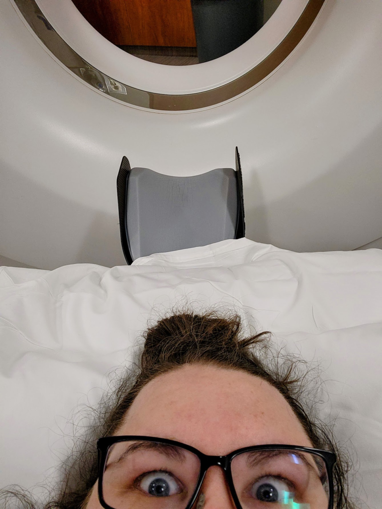 Megan lying on the CT bed waiting to find out if she's going to get the CT. The machine is behind her at the top of the photo.
