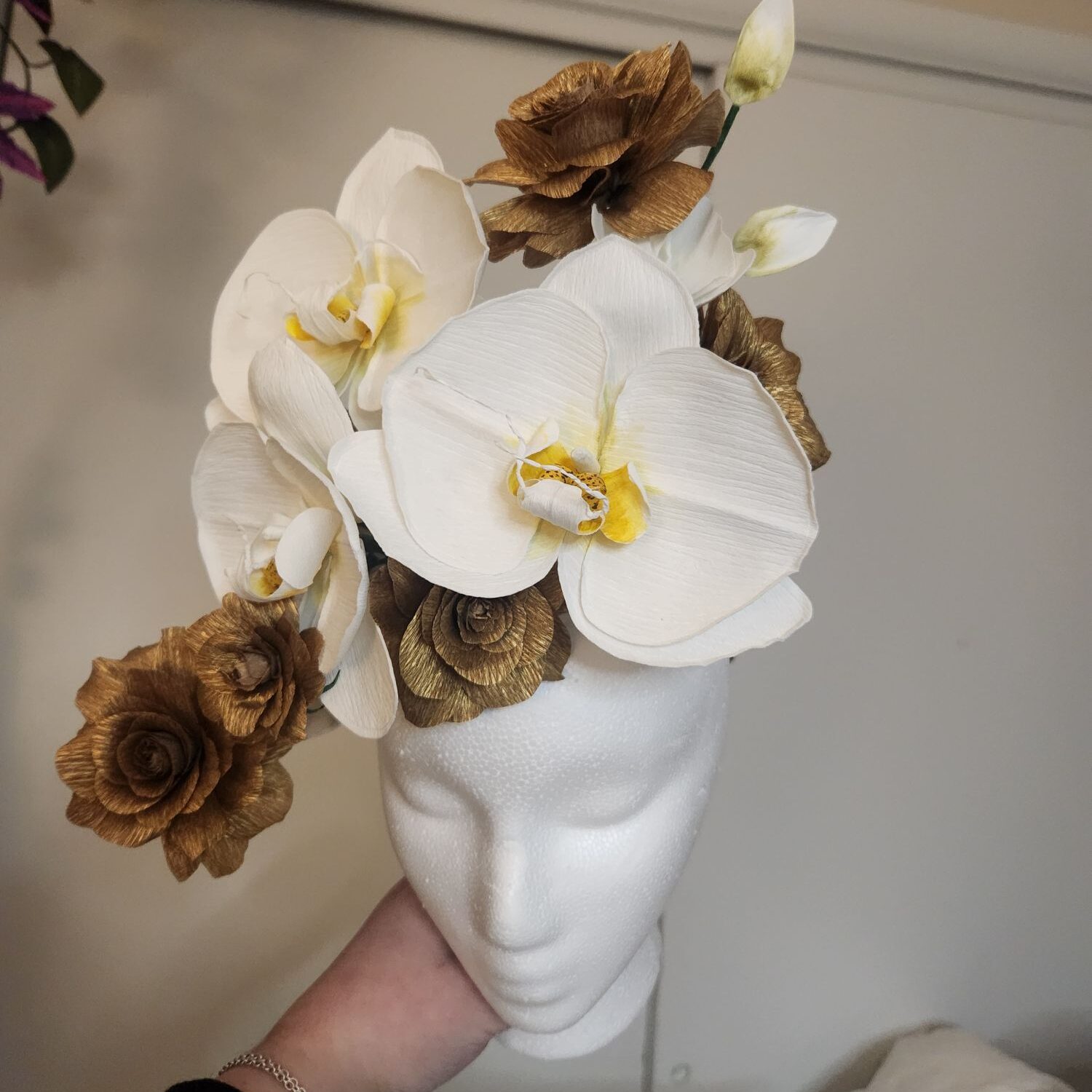 White Orchids and Gold roses sit on a mannequin head.