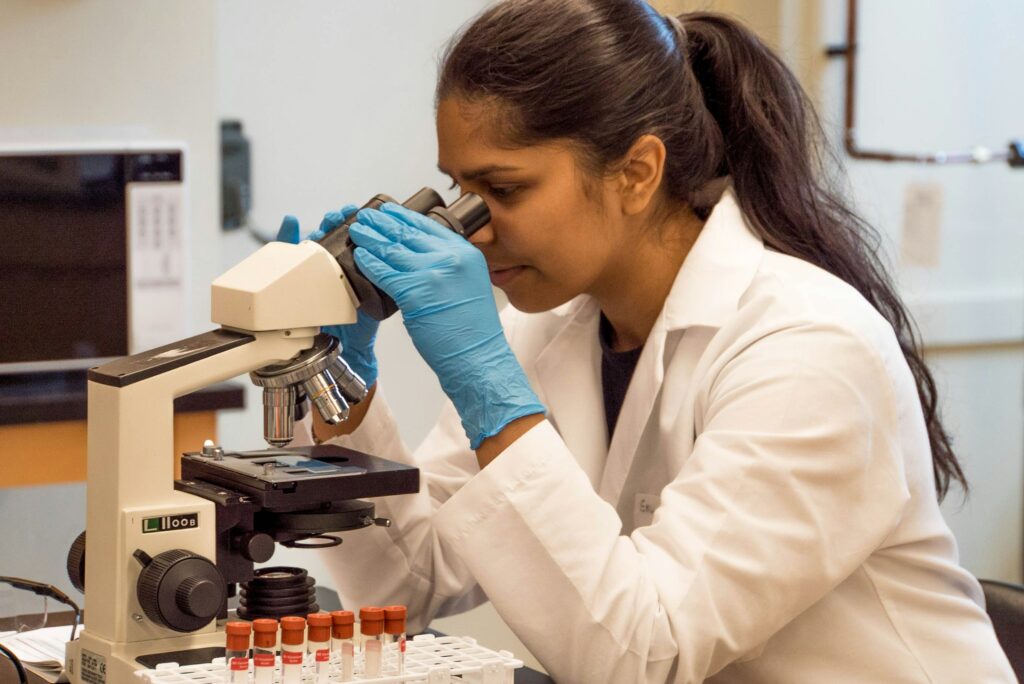 Woman wearing a white lab coat looking into a microscope