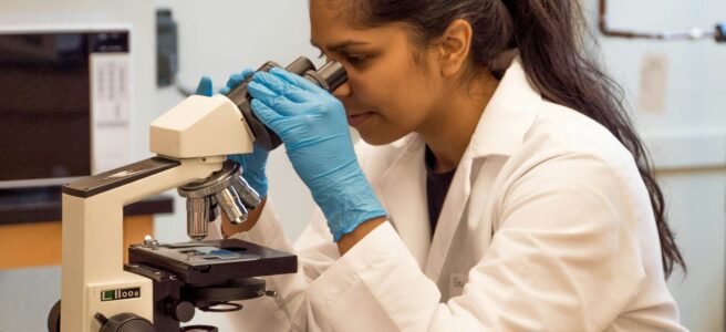 woman wearing a white lab coat looking into a microscope